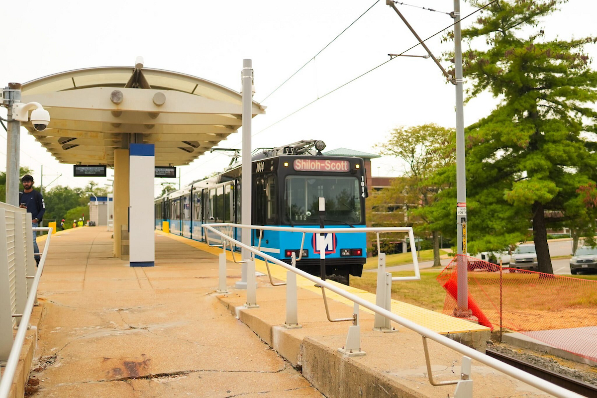 A MetroLink train passes through UMSL North Station with construction fencing nearby.